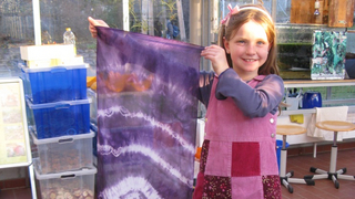 Ein Mädchen hält strahlend ein lilafarbenes Seidentuch hoch.