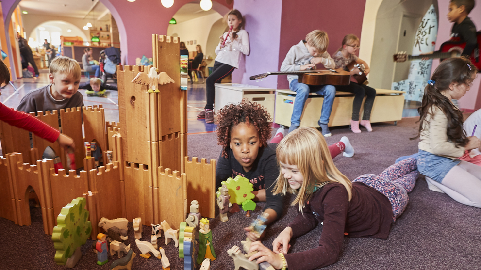 Kinder im Krokoseum bauen ein Schloss aus Holzteilen, spielen Instrumente oder mit Puppen. 