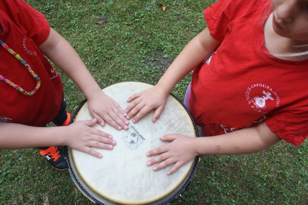 Zwei Kinder schlagen mit ihren Händen auf eine Trommel.