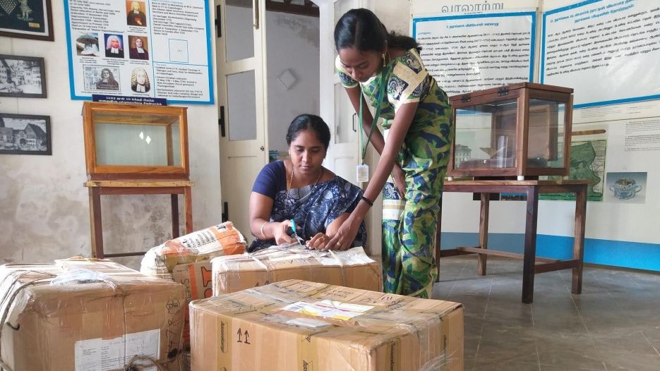 Zwei Mitarbeiterinnen des Museums für den interkulturellen Austausch in Tharangambadi packen große Pakete mit Ausstellungsobjekten aus.