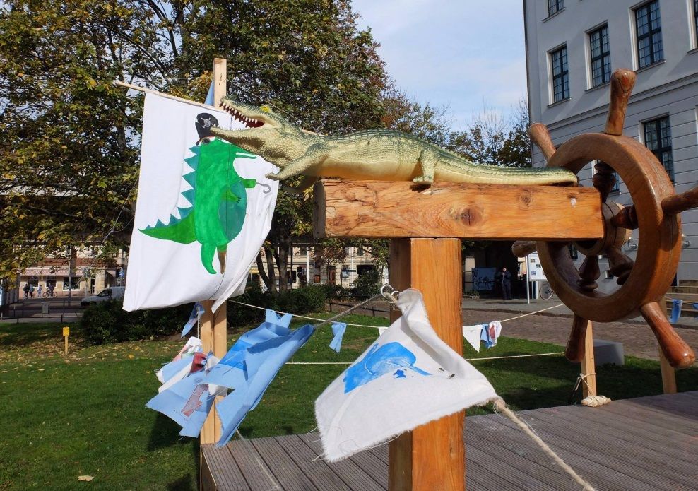 Auf dem Franckeplatz steht ein fantasievoll gestaltetes Schiff: Vor dem Steuerrad sitzt ein Krokodil, bunte Wimpel wehen im Wind und auf dem Segel ist ein Piratenkrokodil gemalt