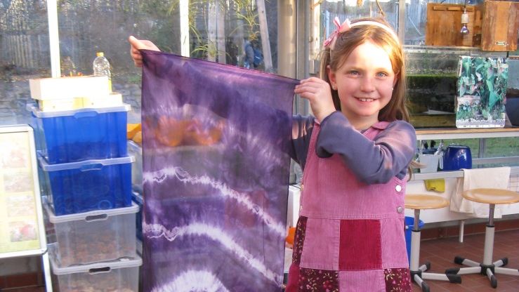 A smiling girl proudly holding up a bright purple silk scarf