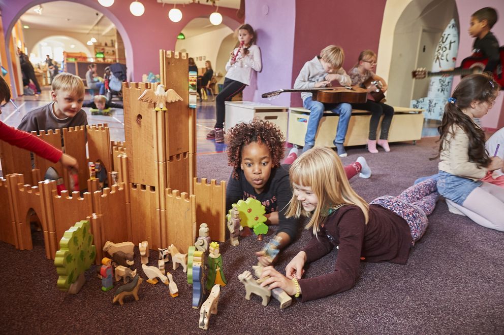 Kinder im Krokoseum spielen frei und fantasievoll: Sie bauen ein Schloss aus Holzteilen, musizieren mit Instrumenten oder spielen mit Puppen