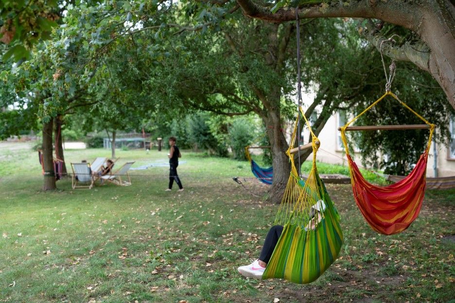 Young people relax in hanging chairs and deckchairs on the green orchard meadow at Stiftsgut Stichelsdorf – surrounded by nature.
