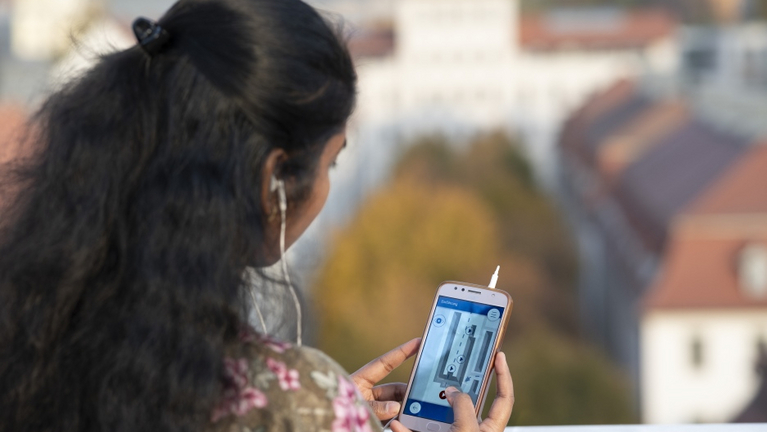 Eine BEsucherin steht auf dem Altan des Historischen Waisenhauses und hörtauf Ihrem Handy im Audioguide Informationen zum Lindenhof an. 