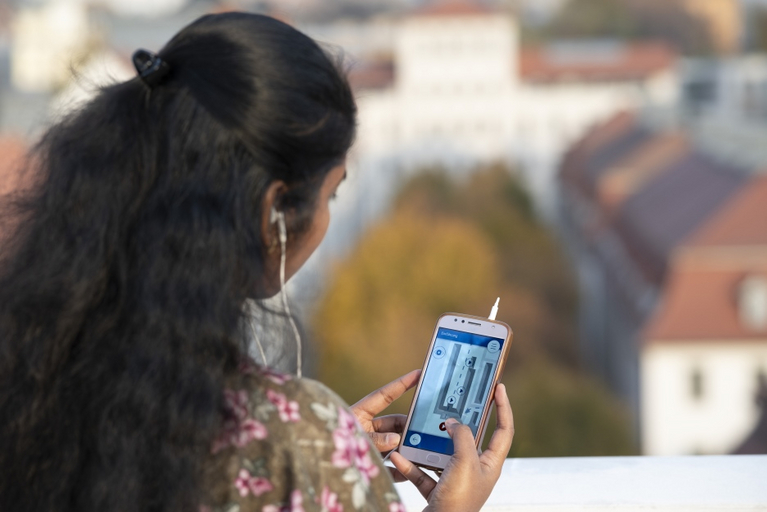 Eine BEsucherin steht auf dem Altan des Historischen Waisenhauses und hörtauf Ihrem Handy im Audioguide Informationen zum Lindenhof an. 
