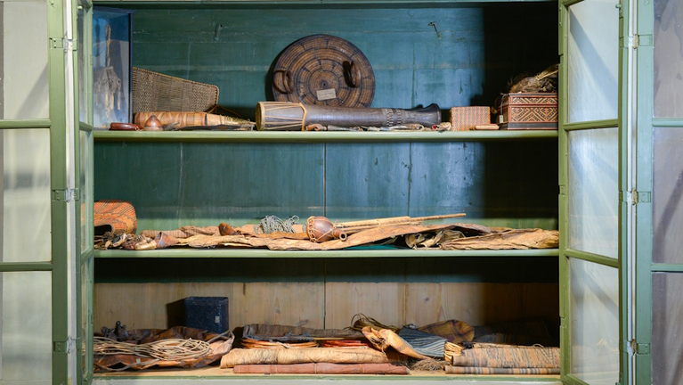 Geöffneter alter Schrank mit Glastüren, in dem sich verschiedene Gegenstände indigener Menschen der südostasiatischen Insel Borneo befinden