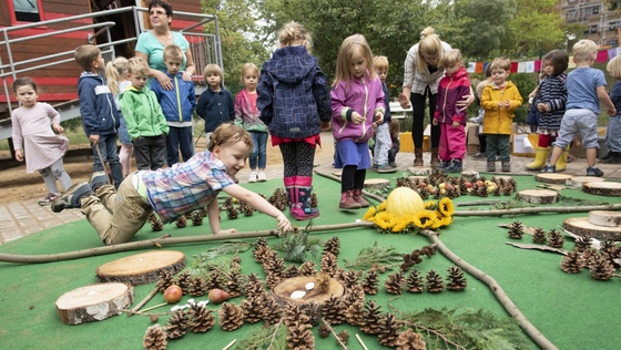 Kinder legen gemeinsam ein riesiges Mandala aus Naturmaterialien wie Sonnenblumen, Zapfen, Holz und Blättern.