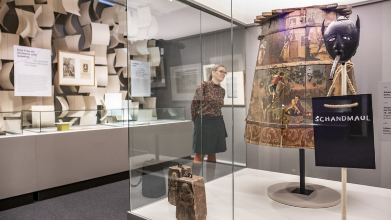 Blick in den Ausstellungsraum "Marktplatz" mit einer historischen Bestrafungsinstrumenten: einer Schandmaske und einem Schandmantel.