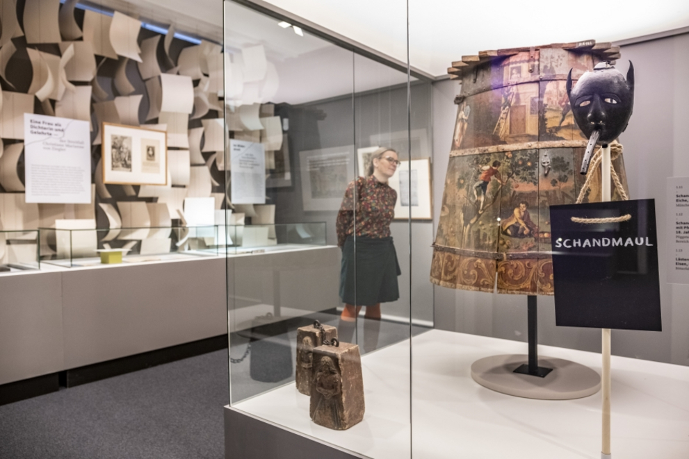 View into the exhibition room "Marktplatz" with a historical instrument of punishment: a shame mask and a shame coat.