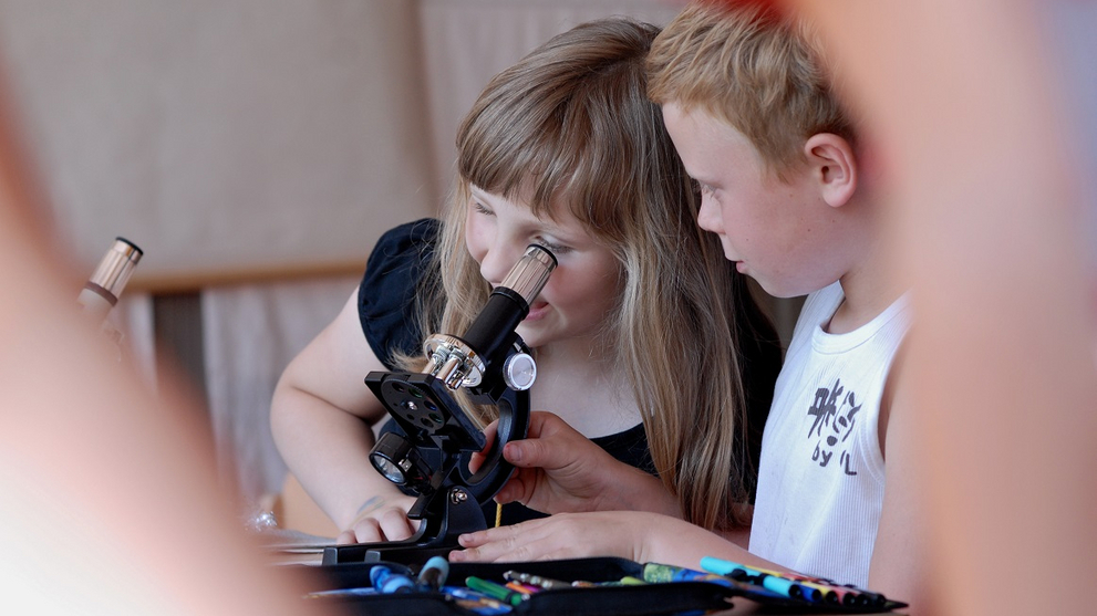 A boy and a girl are experimenting with a microscope.
