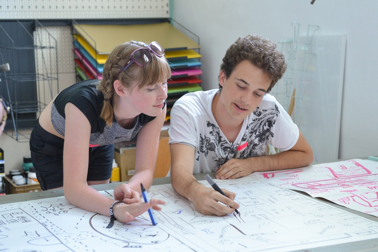 Eine Junge und ein Mädchen beugen sich über ein großes Blatt Papier und planen ein gemeinsames Projekt.
