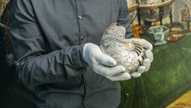 Ein Kurator hält ein verziertes Objekt aus der Wunderkammer in den Händen.