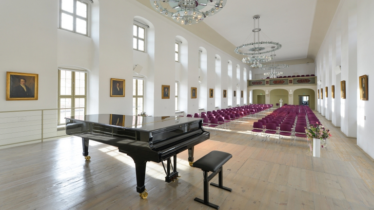 Ansicht des Festaals in den Franckeschen Stiftungen von der Bühne aus. Im Steinway Flügel spiegeln sich die Porträts der Stiftungsdirektoren an der Wand. S