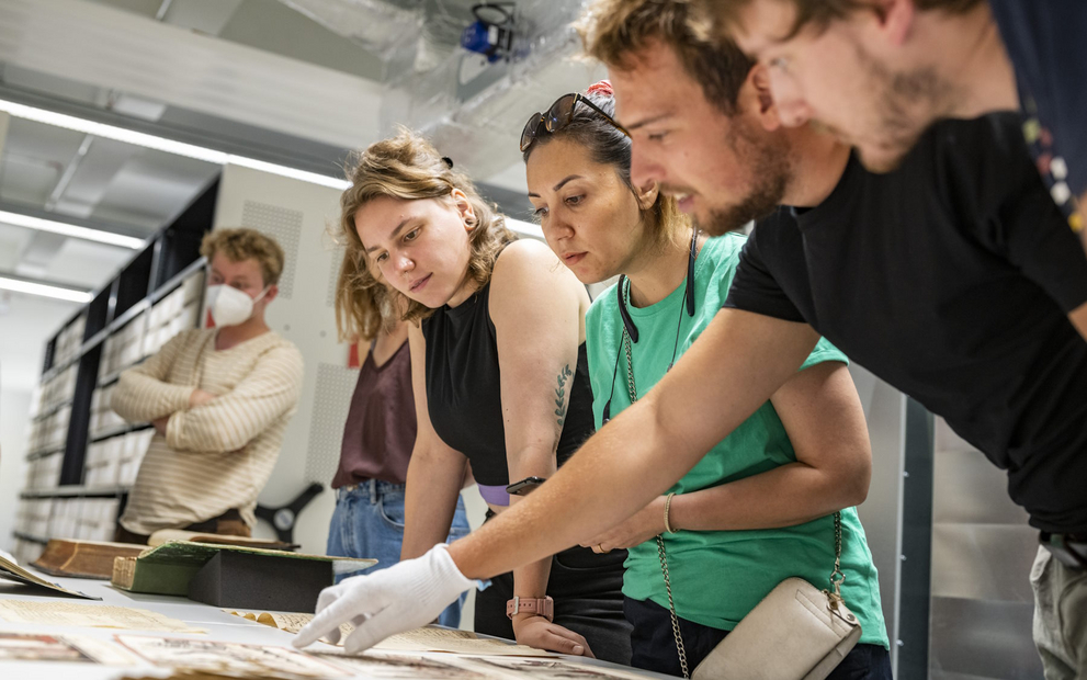 Junge Menschen stehen gemeinsam an einem Tisch und betrachten alte Archivquellen