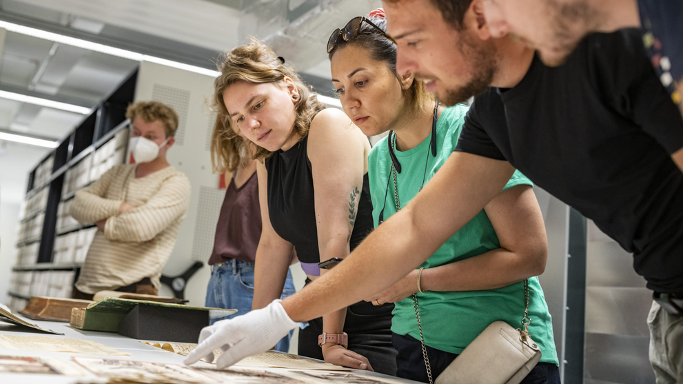 Junge Menschen stehen gemeinsam an einem Tisch und betrachten alte Archivquellen