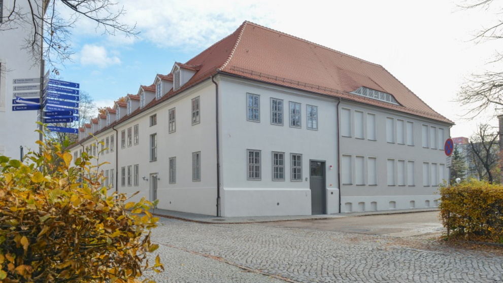 Das frisch sanierte, helle Druckereigebäude leuchtet vor herbstlicher Kulisse.