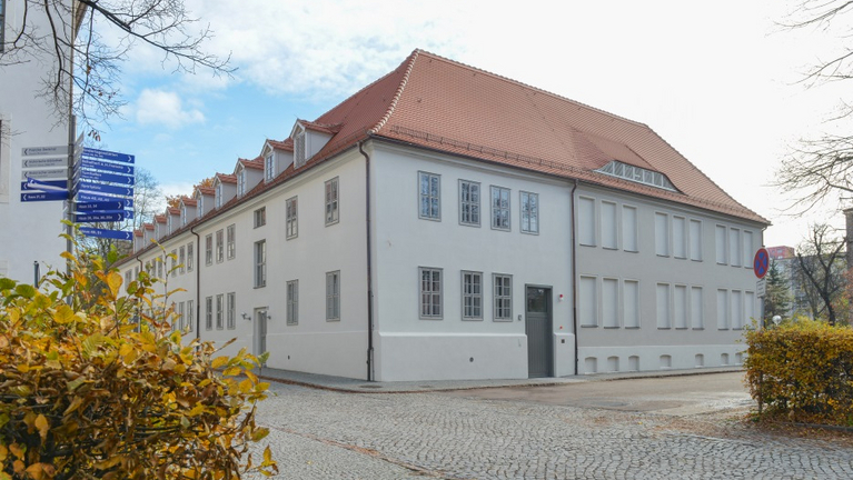 Das frisch sanierte, helle Druckereigebäude leuchtet vor herbstlicher Kulisse.