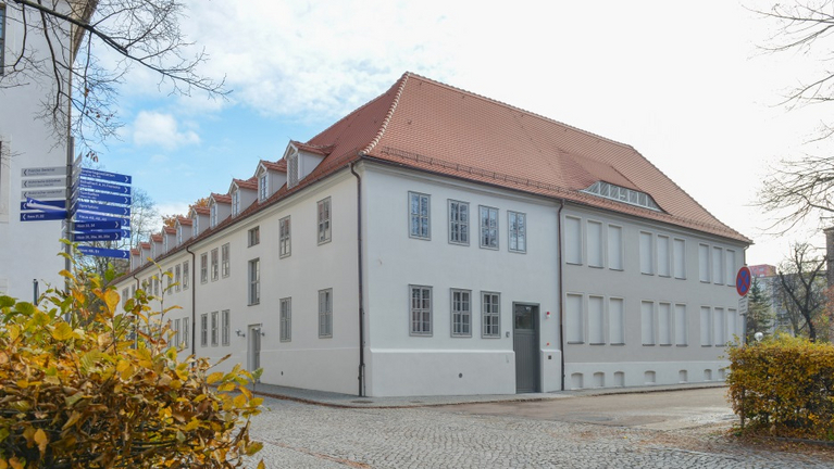 Das frisch sanierte, helle Druckereigebäude leuchtet vor herbstlicher Kulisse.