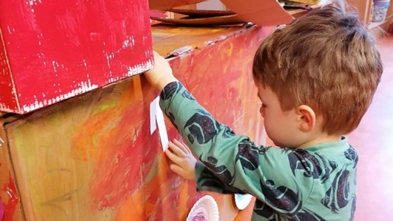 Kind bemalt einen Karton mit roter Farbe 