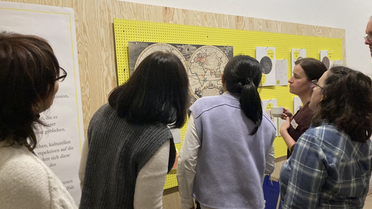 Visitors in the exhibition “Weltblicke” discuss the placement of their present-day countries of origin in front of an 18th-century world map.