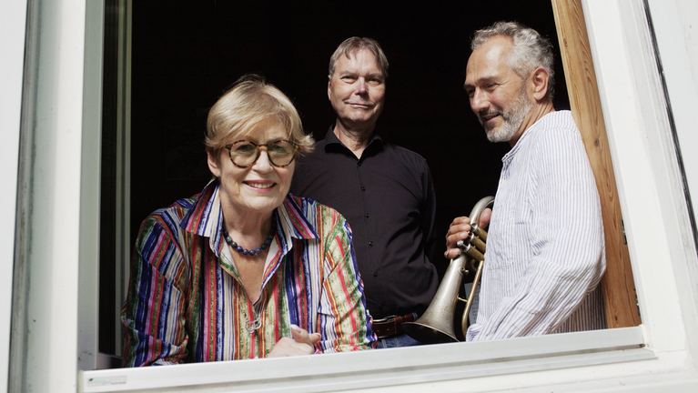 Drei Musiker:innen schauen aus dem Fenster