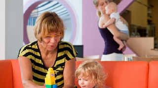 Eine Familienpatin betreut das Kleinkind, während die Mutter sich um den Säugling kümmert.