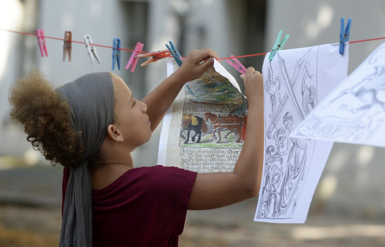 A girl hangs paper artwork on a clothesline to dry. They flutter in the wind.