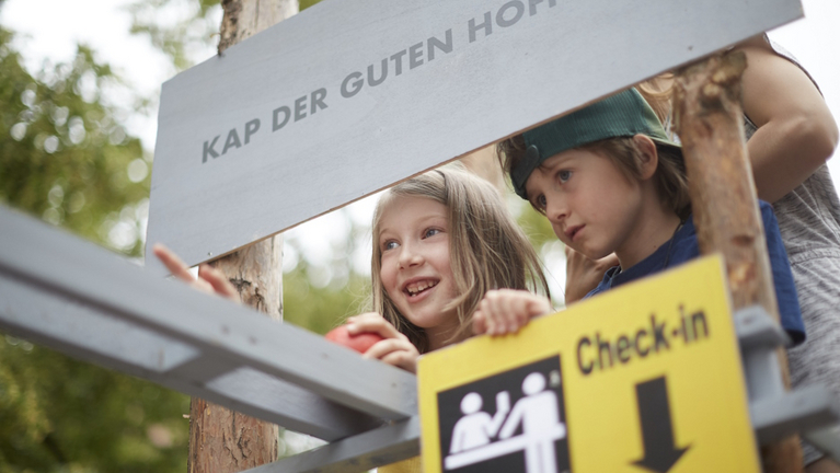 Drei Kinder spielen Schiffsreise auf einer Kunstinstallation aus Holzlatten auf dem Lindenblütenfest.
