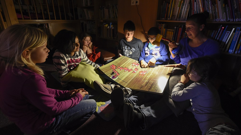 Kinder lesen in der gemütlich-dunklen Bibliothek mit der Taschenlampe gemeinsam ein Buch. 
