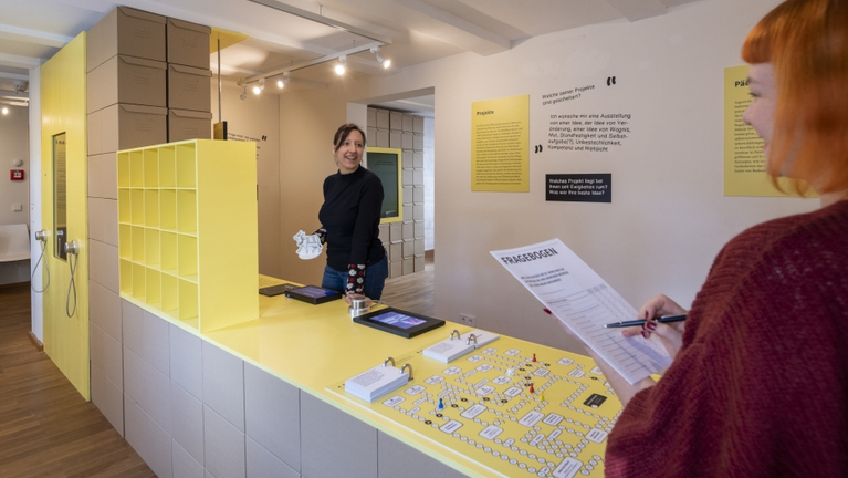 Zwei Besucherinnen füllen in einem Ausstellungsraum den Fragebogen zur Mitmach-Ausstellung aus. 