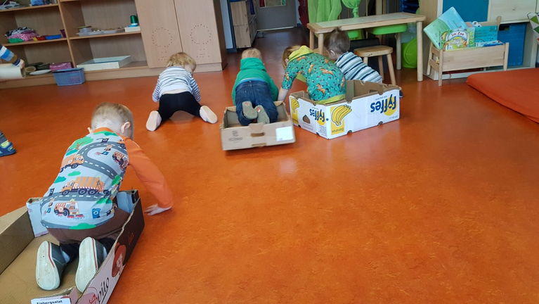 mehrere Kinder rutschen mit Kartons durch den Raum