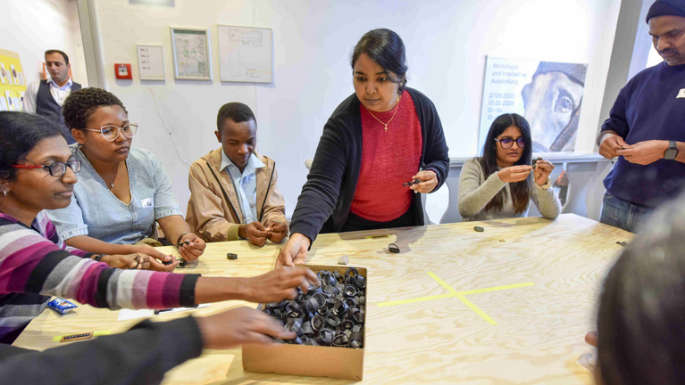 Teilnehmende arbeiten kreativ mit Materialien an einem großen Tisch