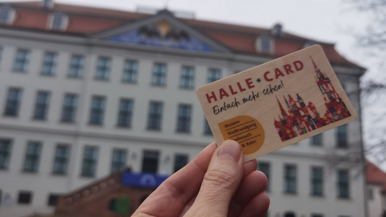 Eine Hand hält die Halle Card, im Hintergrund das Historische Waisenhaus